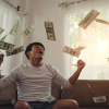 A young man throwing money in the air while sitting on the couch.