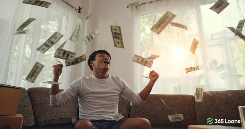 A young man throwing money in the air while sitting on the couch.